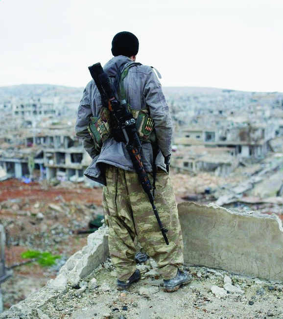 FILE - In this Jan. 30, 2015 file photo, a Syrian Kurdish sniper looks at the rubble in the Syrian city of Ain al-Arab, also known as Kobani. Foreign fighters are streaming in unprecedented numbers to Syria and Iraq to battle for the Islamic State or other U.S. foes, including at least 3,400 from Western nations and 150 Americans, U.S. intelligence officials conclude. In all, more than 20,000 fighters have traveled to Syria from more than 90 countries, top intelligence officials will tell Congress this week.  (AP Photo, File) Islamic State Foreign Fighters