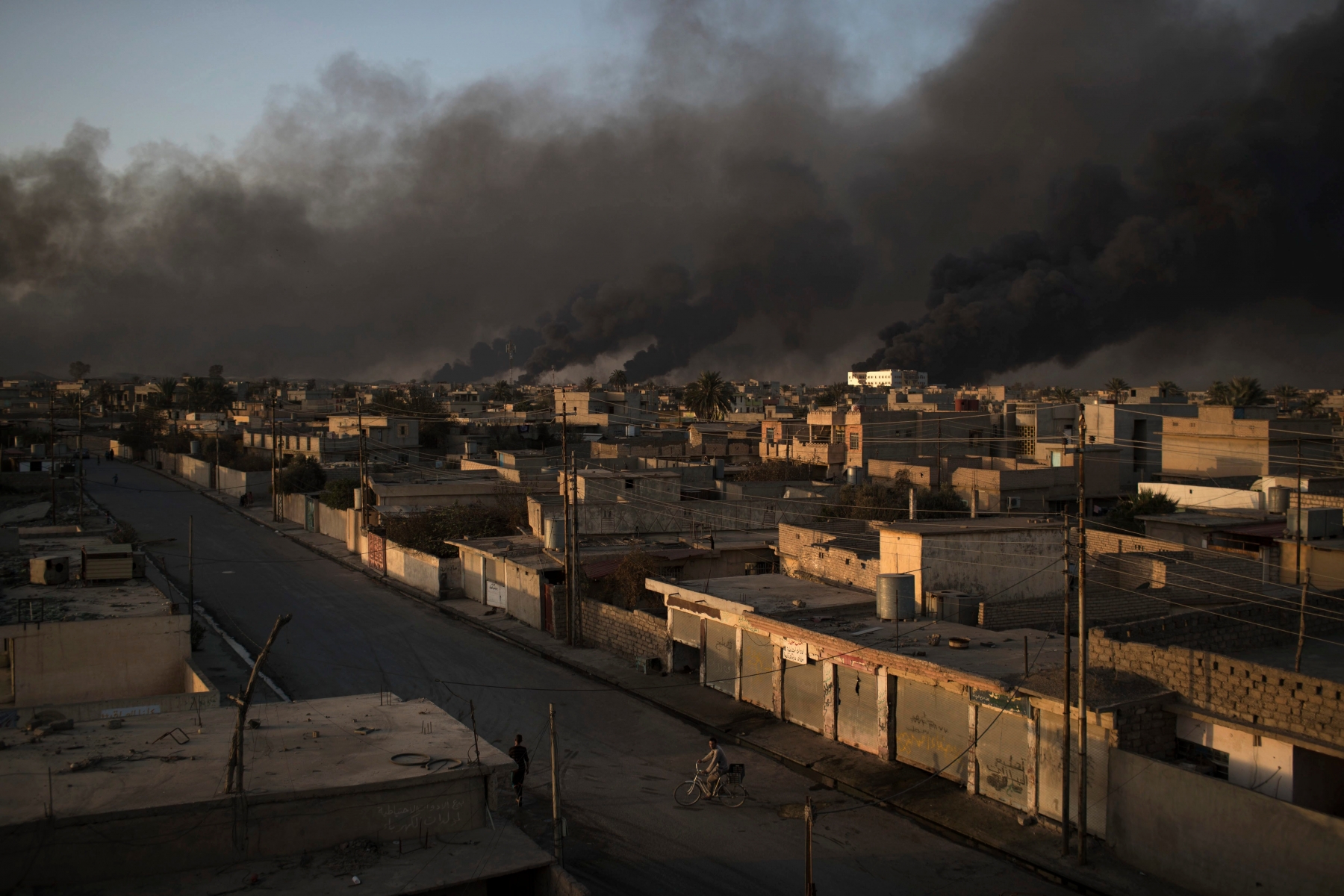 A man rides his bike on a street as smoke rises from burning oil fields in Qayara, some 50 kilometers south of Mosul, Iraq, Monday, Oct. 31, 2016. For two weeks, Iraqi forces and their Kurdish allies, Sunni tribesmen and Shiite militias have been converging on Mosul from multiple directions to drive Islamic State militants from Iraq's second largest city. (AP Photo/Felipe Dana) APTOPIX Mideast Iraq Mosul