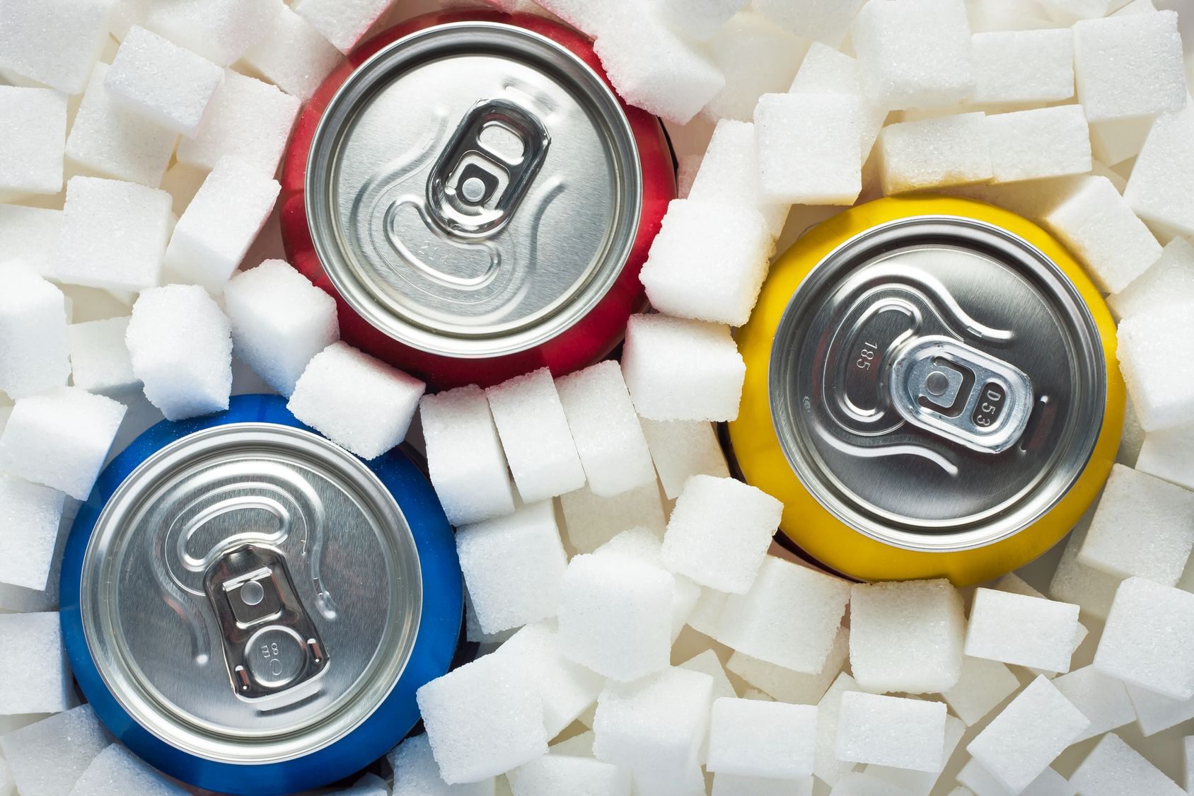 Unhealthy food concept - sugar in carbonated drinks. Sugar cubes as background and canned drinks  Sugar in food