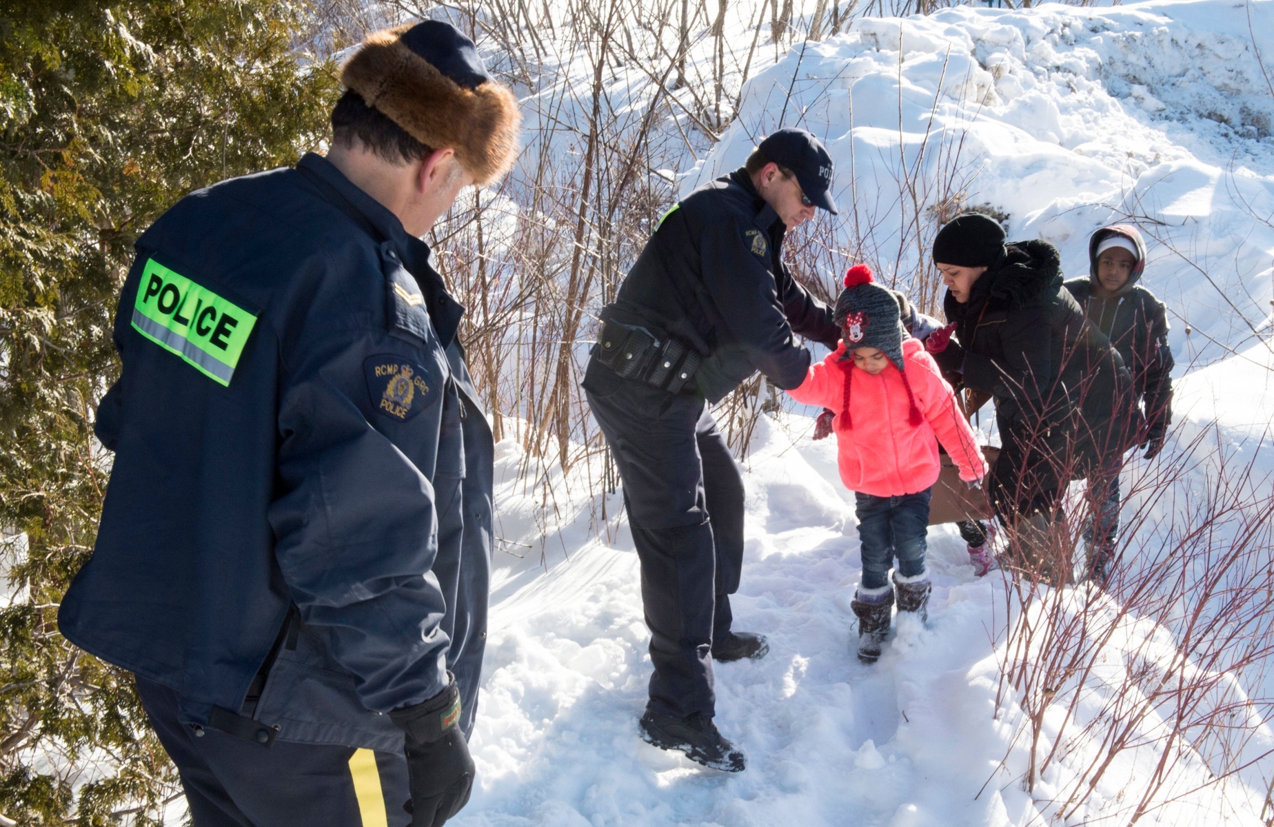 Family members from Somalia are helped into Canada by RCMP officers along the U.S.-Canada border near Hemmingford, Quebec, on Friday, Feb. 17, 2017. A number of refugee claimants are braving the elements to illicitly enter Canada. (Paul Chiasson/The Canadian Press via AP) Canada US Border Refugees