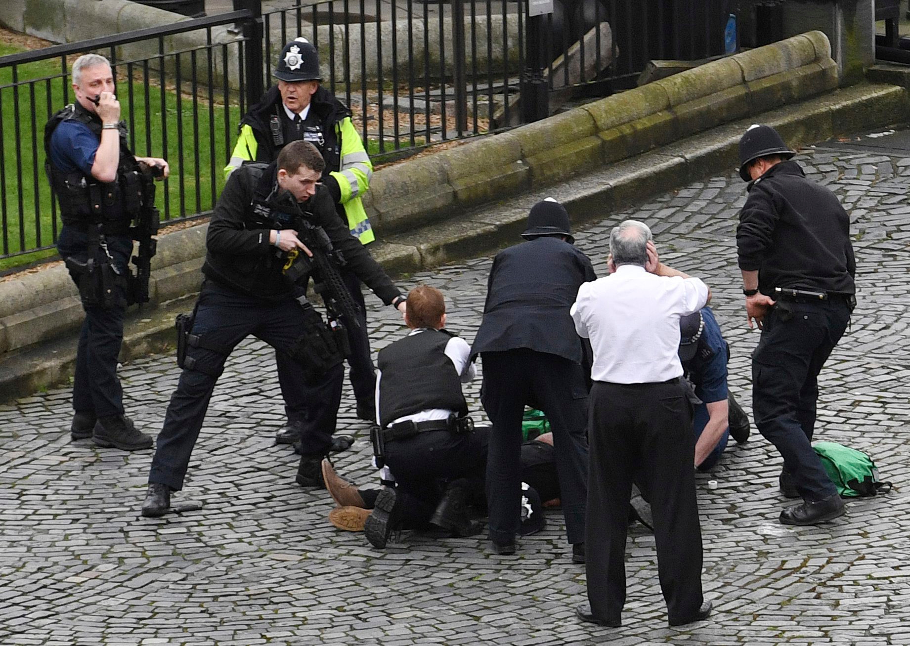 A policeman points a gun at a man on the floor as emergency services attend the scene outside the Palace of Westminster, London, Wednesday, March 22, 2017.  London police say they are treating a gun and knife incident at Britain's Parliament "as a terrorist incident until we know otherwise." The Metropolitan Police says in a statement that the incident is ongoing. It is urging people to stay away from the area. Officials say a man with a knife attacked a police officer at Parliament and was shot by officers. Nearby, witnesses say a vehicle struck several people on the Westminster Bridge.  (Stefan Rousseau/PA via AP). APTOPIX Britain Parliament Incident
