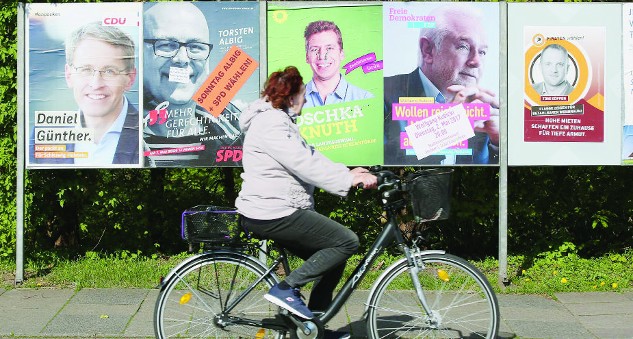 Eine Passantin fährt am 07.05.2017 in Eckernfoerde (Schleswig-Holstein) bei der Landtagswahl in Schleswig-Holstein mit ihrem Fahrrad an Wahlplakaten entlang, auf dene die Spitzenkandidaten der Parteien zu sehen sind. (KEYSTONE/dpa/Bodo Marks) DEUTSCHLAND LANDTAGSWAHLEN