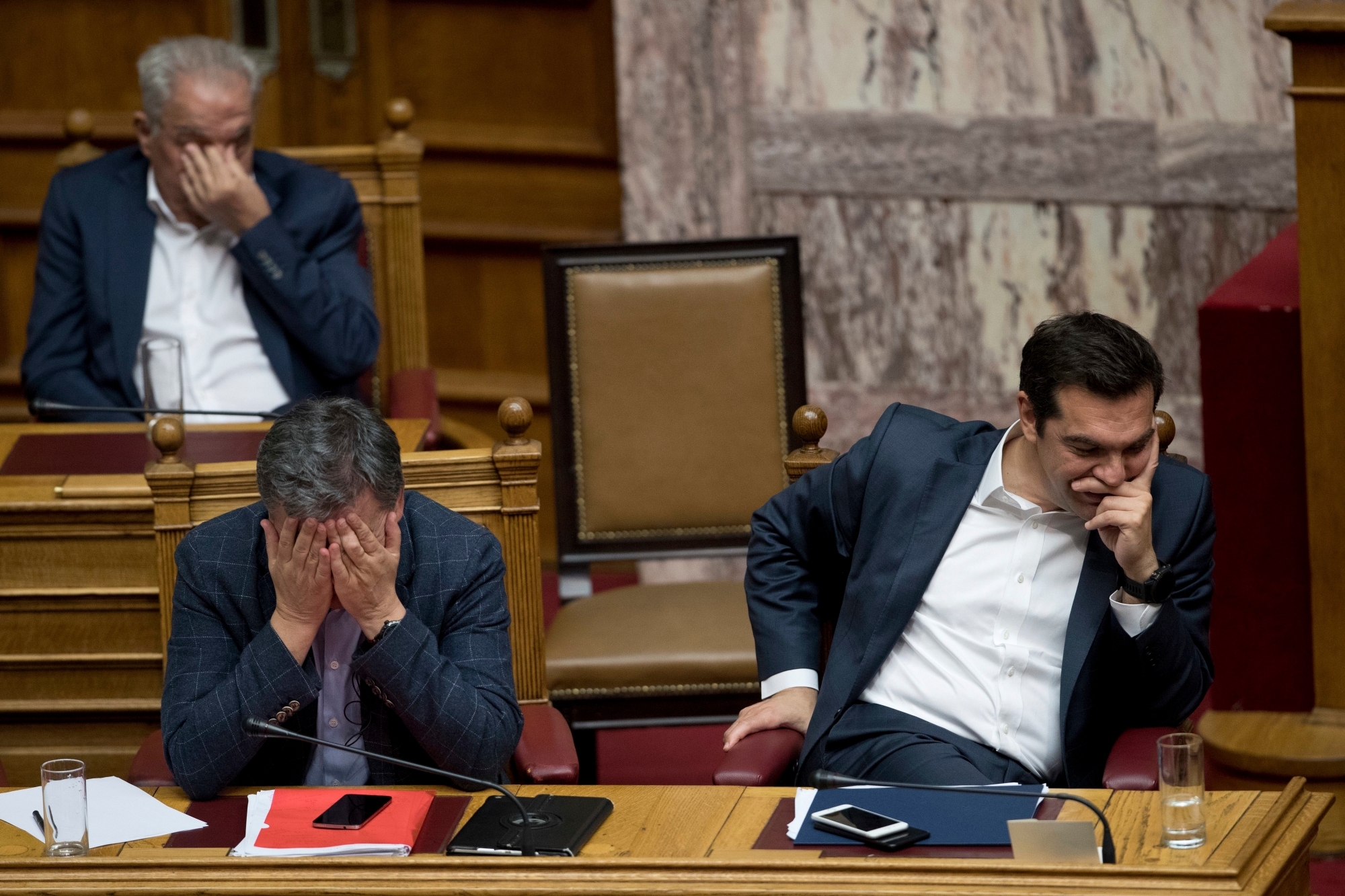 Greek Finance Minister Euclid Tsakalotos, left, and Greece's Prime Minister Alexis Tsipras, right, react during a parliamentary session to vote more austerity measures as part of an agreement with international bailout creditors, in Athens, Thursday, may 18, 2017. Protesters clashed with police in central Athens during a second day of demonstrations Thursday, as lawmakers prepared to vote on creditor-demanded measures that will usher in additional income losses for Greeks over the next three years.(AP Photo/Petros Giannakouris) Greece Bailout