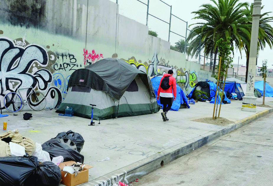 A pedestrian walks past a homeless encampment alongside a street in downtown Los Angles on Wednesday, May 31, 2017. The number of homeless people counted in Los Angeles County has jumped 23 percent, quadrupling the percentage increase from a year earlier. The Los Angeles Homeless Services Authority said Wednesday that its annual count in January found 57,794 homeless in the county with a population of 10 million. That's up from about 46,800 in January 2016 and 44,300 in 2015. (AP Photo/Richard Vogel) LOS ANGELES HOMELESS