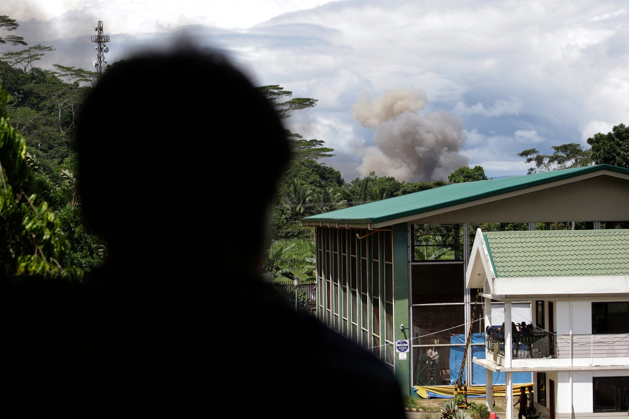 In this Friday, June 9, 2017, photo, an evacuee looks as black smoke rises from continuing military air strikes outside a temporary evacuation center at the provincial government capitol in Marawi city, southern Philippines. Nearly every day for the past three weeks, the Philippine military has pounded the lakeside town of Marawi with rockets and bombs as it tries to wipe out militants linked to the Islamic State group in some of the most protracted urban combat to hit this volatile region in decades. (AP Photo/Aaron Favila) Philippines A Window To War