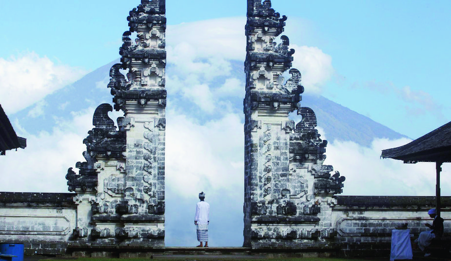 Balinese man watches Mount Agung volcano almost covered with clouds as he stands at a temple in Karangasem, Bali, Indonesia, Tuesday, Sept. 26, 2017. An increasing frequency of tremors from the volcano indicates magma is continuing to move toward the surface and an eruption is possible, a disaster agency official said Tuesday. Tourists are cutting short their stay to the island, where an eruption would force the airport to close and strand thousands. (AP Photo/Firdia Lisnawati) APTOPIX Indonesia Bali Volcano