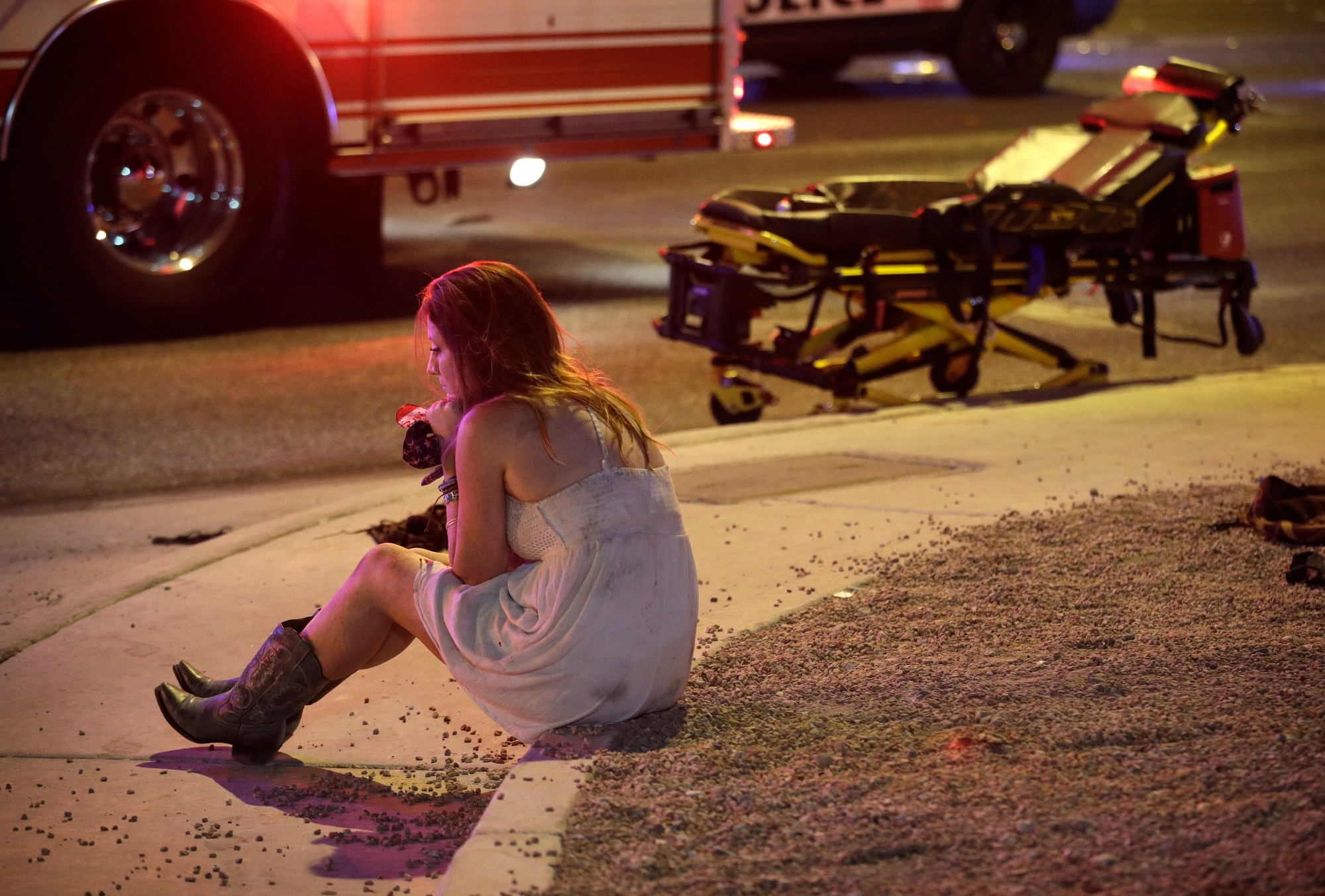 A woman sits on a curb at the scene of a shooting outside of a music festival along the Las Vegas Strip, Monday, Oct. 2, 2017, in Las Vegas. Multiple victims were being transported to hospitals after a shooting late Sunday at a music festival on the Las Vegas Strip. (AP Photo/John Locher) Las Vegas Shooting