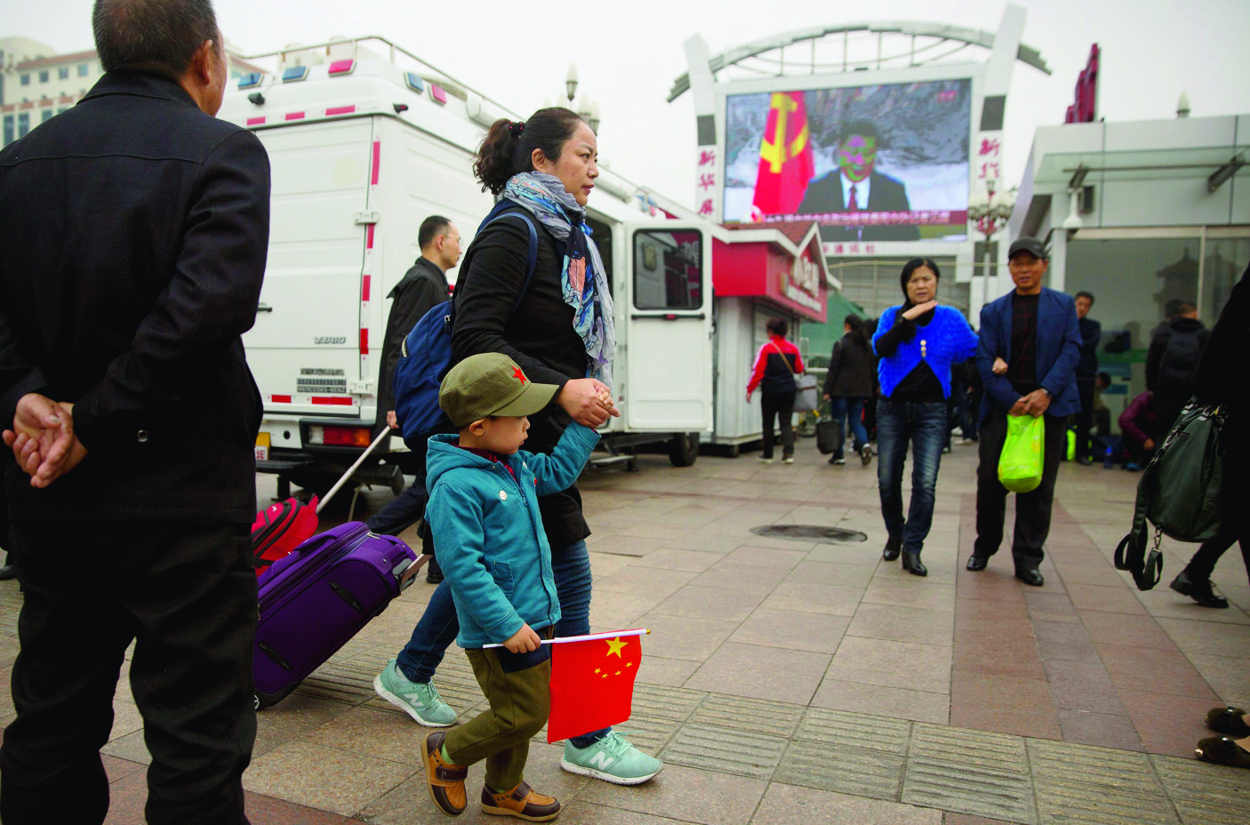 A woman and a boy carrying a Chinese flag walk past a television screen outside of the Beijing Railway Station showing a live broadcast of Chinese President Xi Jinping introducing members of the Politburo Standing Committee of China's 19th Party Congress at the Great Hall of the People in Beijing, Wednesday, Oct. 25, 2017. Communist Party leader Xi Jinping on Wednesday unveiled the lineup of the party's highest body who will rule alongside him as he embarks on a second five-year term as party leader. (AP Photo/Mark Schiefelbein) China Party Congress