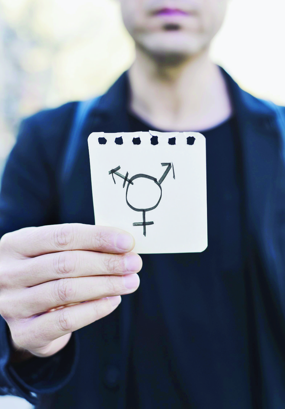 closeup of a young Caucasian man in the street showing a piece of paper with a transgender symbol drawn in it man and transgender symbol