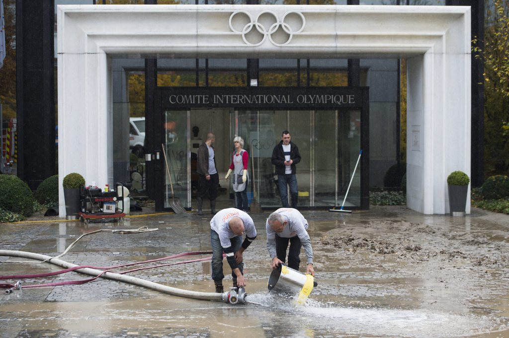 Deux ouvriers enlèvent la boue et l'eau devant l'entrée du siège principale du Comité International Olympique.