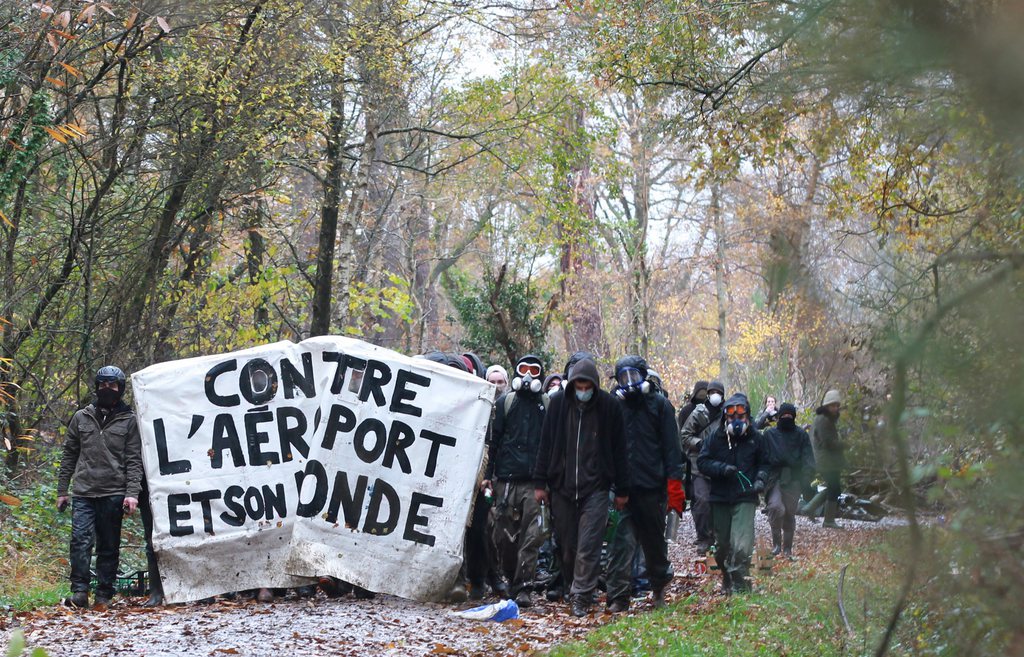 Activists walks in a wooded area of the site of the planned Notre-Dame-Des-Landes of western France  on Friday Nov 23, 2012. In a muddy, rainy standoff starting early Friday, protesters responded to police attempts to remove them by hurling sticks, stones and gasoline bombs. For two weeks, protesters have illegally occupied the site of the planned Notre-Dame-Des-Landes airport set to start operating in 2017. the banners is read " against it's airport and it's world" (AP Photo/Laetitia Notarianni)