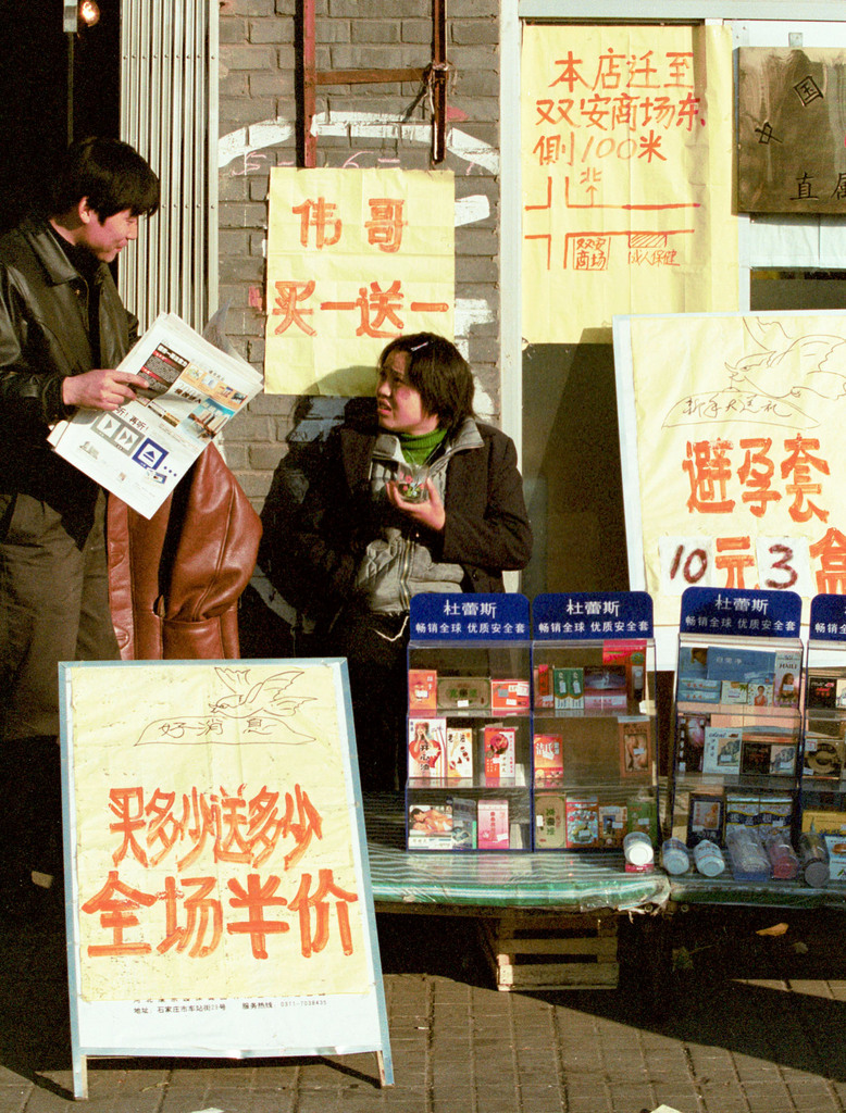 A vendor sits by a display of condoms and sale signs outside a sex shop which is about to be demolished, in Beijing Friday January 12, 2001. The signs offer big discounts for products at the store, including a "buy one, get one free" deal for Viagra. It was not clear whether the Viagra was the real product or one of many fakes which use the same name. (KEYSTONE/AP Photo/Str)