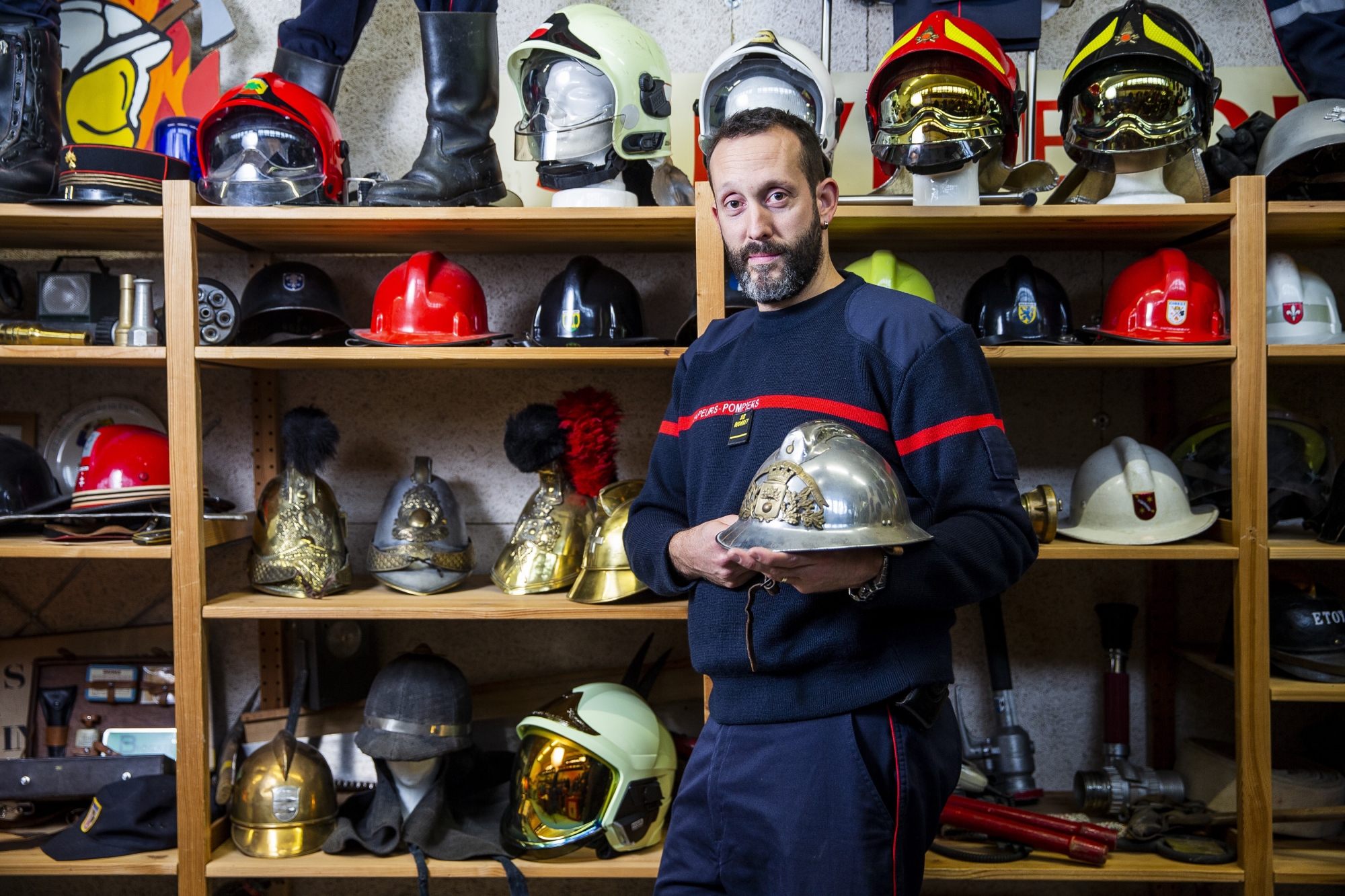 David Pagot entouré d’un échantillon de ses 200 casques de sapeurs-pompiers, provenant essentiellement de Suisse ou de France. Dans ses mains, le premier casque qu’il a porté en devenant pompier volontaire dans la commune française où il a grandi.