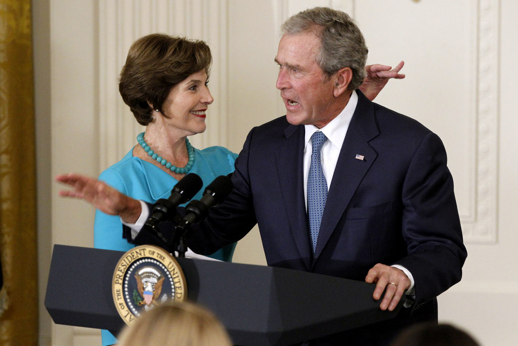 Former President George W. Bush, accompanied by former first lady Laura Bush, motions for audience members to sit down, in the East Room of the White House in Washington, Thursday, May 31, 2012, during a ceremony to unveil their official portraits. (AP Photo/Charles Dharapak)