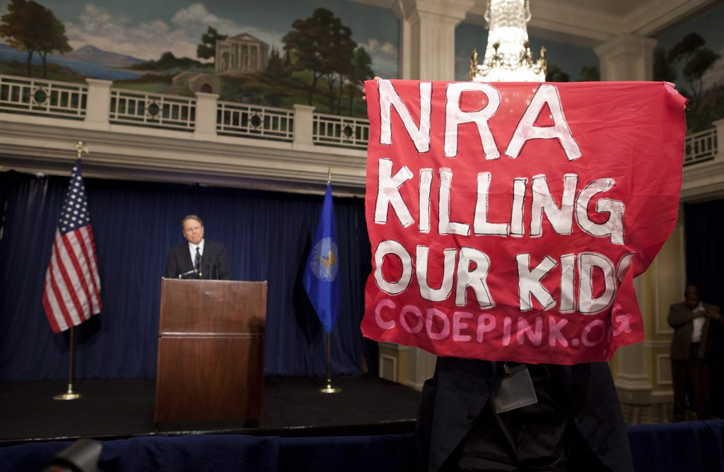 A protester holds up a sign as National Rifle Association executive vice president Wayne LaPierre, left, speaks during a news conference in response to the Connecticut school shooting on Friday, Dec. 21, 2012 in Washington.  (AP Photo/ Evan Vucci)