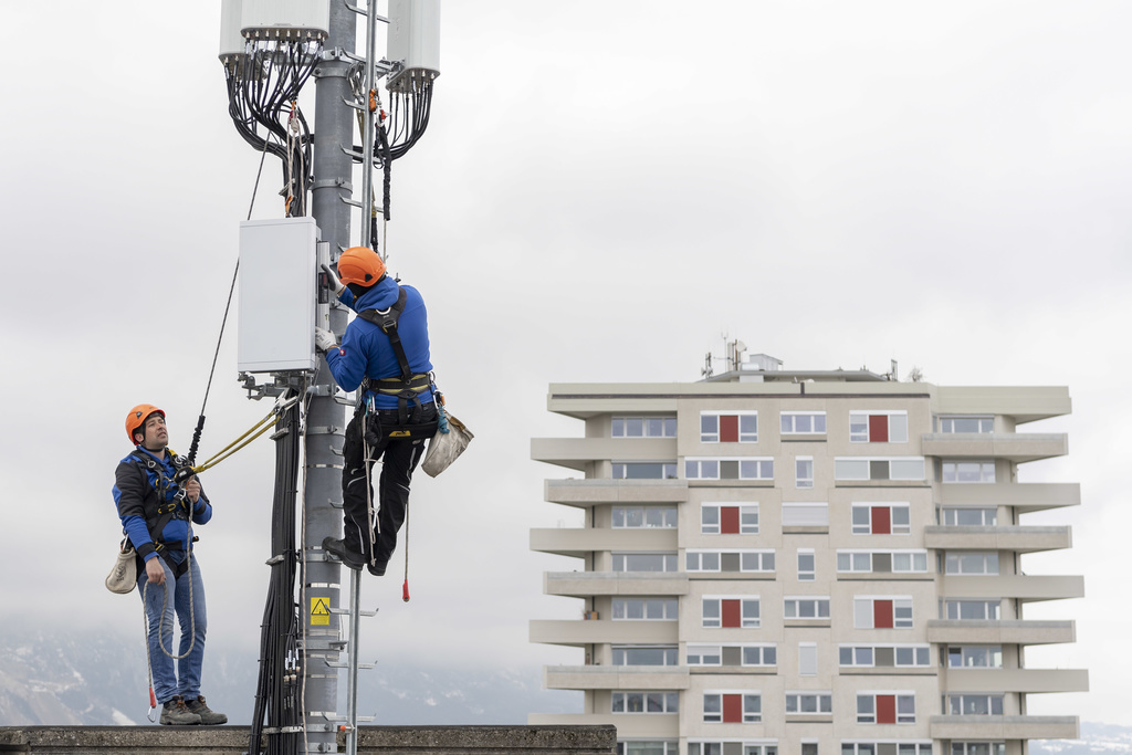Deux employes de l'entreprise Axians installent une antenne 5G de communication pour les mobiles sur un mat situe sur le toit d'un immeuble du quartier de la Gradelle a Chene-Bougeries ce vendredi 5 avril 2019 dans le canton de Geneve. Swisscom tient une conference de presse sur la construction de l'antenne 5G ce mercredi 10 avril 2019 a Zurich. (KEYSTONE/Martial Trezzini)