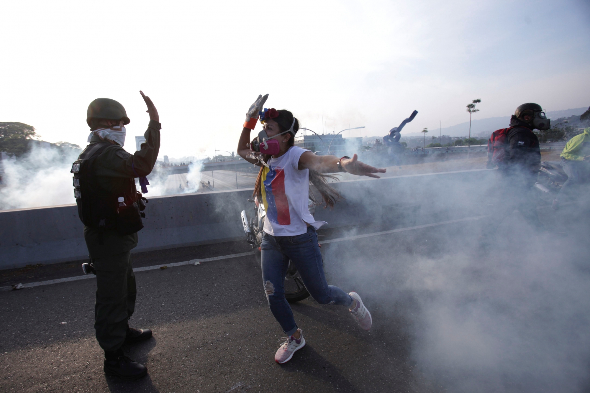 An opponent to Venezuela's President Nicolas Maduro high fives a rebel soldier on a highway overpass outside La Carlota air base amid tear gas fired by loyalist soldiers inside the base in Caracas, Venezuela, Tuesday, April 30, 2019. Venezuelan opposition leader Juan Guaidó took to the streets in Caracas with activist Leopoldo Lopez and a small contingent of heavily armed troops early Tuesday in a bold and risky call for the military to rise up and oust socialist leader Nicolas Maduro. (AP Photo/Boris Vergara) APTOPIX VENEZUELA POLITICAL CRISIS