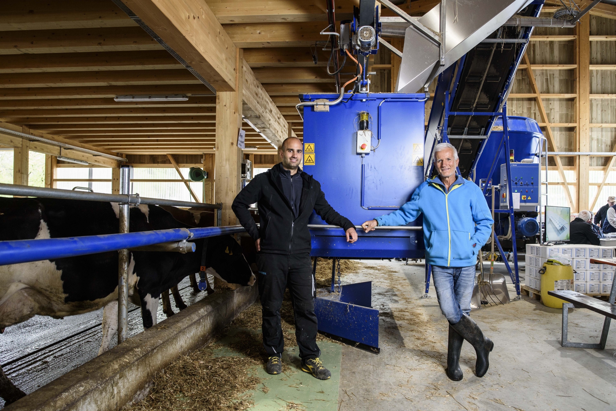 Thibault et Serge Melly devant le robot distribuant le fourage à leurs 60 vaches qui évoluent dans un univers automatisé sur fond de musique classique.