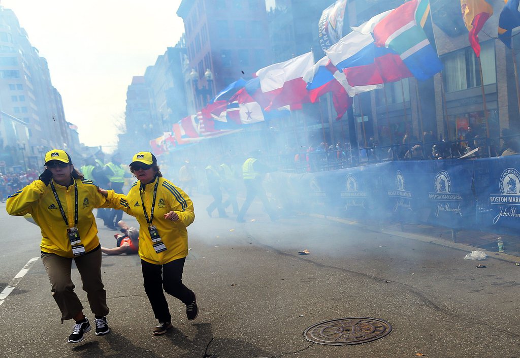 People react to an explosion at the 2013 Boston Marathon in Boston, Monday, April 15, 2013. Two explosions shattered the euphoria of the Boston Marathon finish line on Monday, sending authorities out on the course to carry off the injured while the stragglers were rerouted away from the smoking site of the blasts. (AP Photo/The Boston Globe,  John Tlumacki)  MANDATORY CREDIT