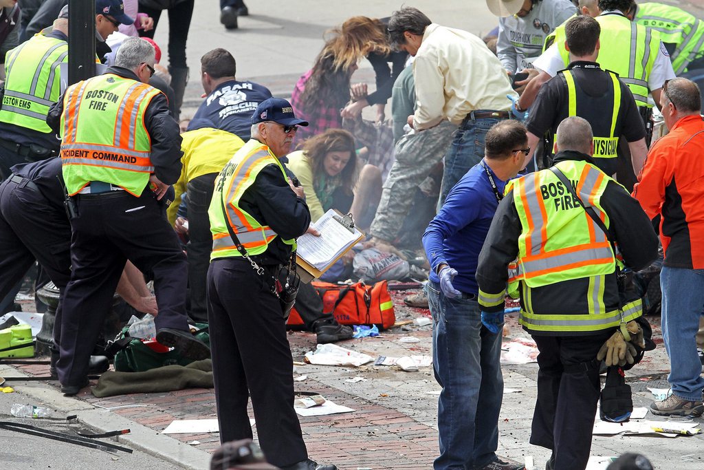 Rescue personnel aid injured people near the finish line of the 2013 Boston Marathon following explosions in Boston, Monday, April 15, 2013. Two explosions shattered the euphoria of the Boston Marathon finish line on Monday, sending authorities out on the course to carry off the injured while the stragglers were rerouted away from the smoking site of the blasts. (AP Photo/The Boston Herald, Stuart Cahill)