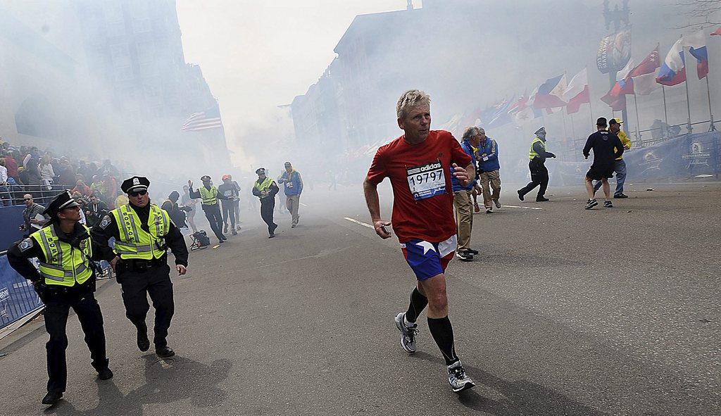 A Boston Marathon competitor and Boston police run from the area of an explosion near the finish line in Boston, Monday, April 15, 2013. (AP Photo/MetroWest Daily News, Ken McGagh)  MANDATORY CREDIT