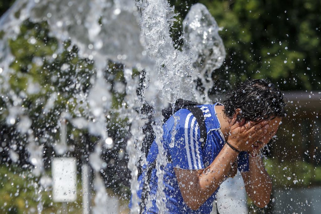 A men cool off with water-jets of the fountain at the Place des Nations in Geneva, during a hot summer day, in Geneva, Switzerland, Saturday, July 20, 2019. (KEYSTONE/Salvatore Di Nolfi)